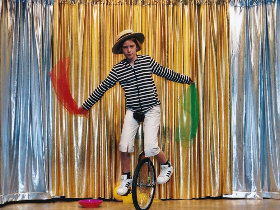 Ein Kind der Zirkus Mitmachshow fährt auf einem Einrad und hat bunte Tücher in der Hand.